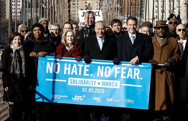 Politicians walk across the Brooklyn Bridge; on the left is Lieutenant Governor Kathy Hochul, Attorney General Tish James, Senator Kirsten Gillibrand, Senator Chuck Schumer, Governor Andrew Cuomo; standing in the background among other marchers is Mayor Bill de Blasio